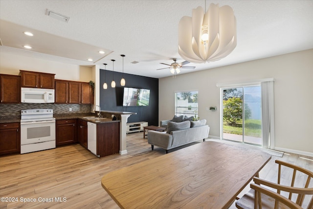 kitchen with kitchen peninsula, light wood-type flooring, white appliances, sink, and pendant lighting