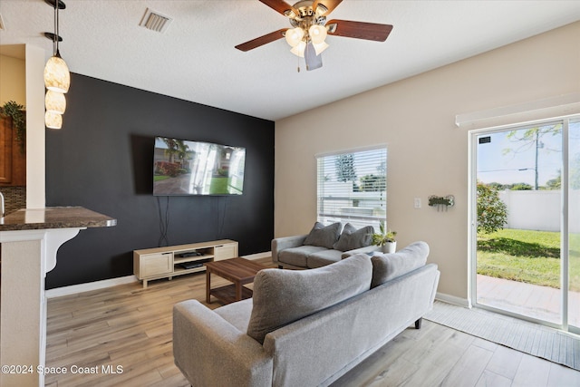 living room with a textured ceiling, light wood-type flooring, and ceiling fan