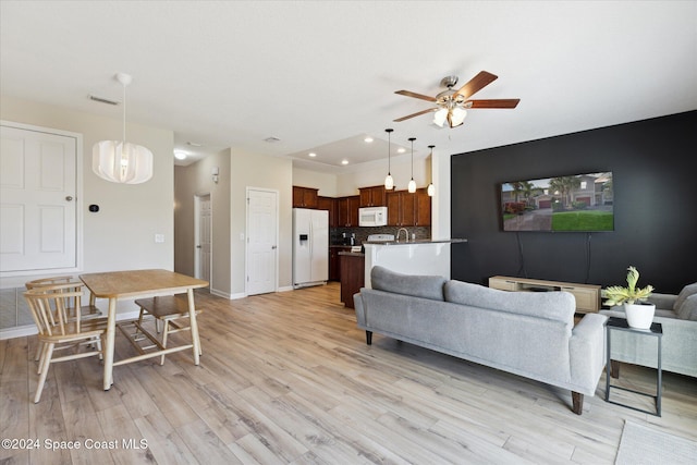 living room with ceiling fan with notable chandelier and light hardwood / wood-style floors