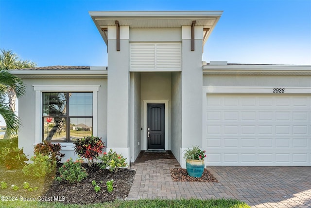 doorway to property featuring stucco siding, decorative driveway, and a garage