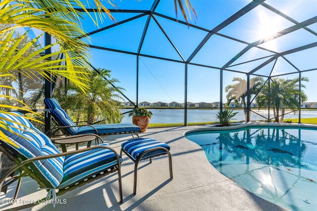 outdoor pool with glass enclosure, a patio, and a water view