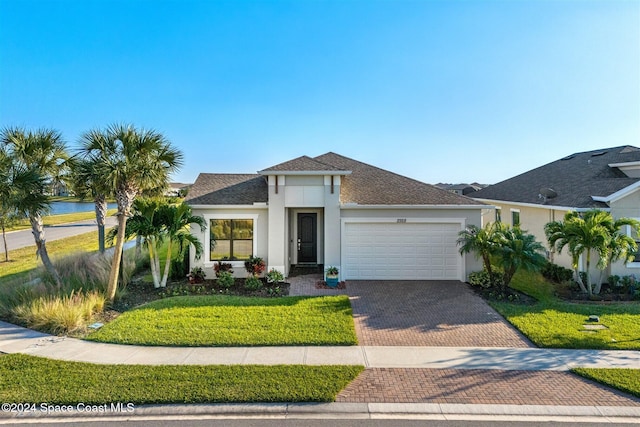 view of front of house featuring a front lawn, roof with shingles, stucco siding, decorative driveway, and an attached garage