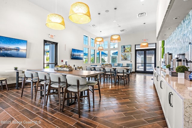 dining space featuring visible vents, a high ceiling, wood tiled floor, and french doors