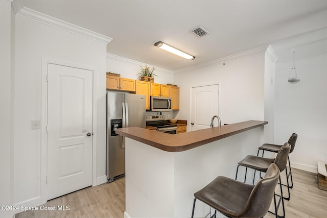 kitchen featuring hanging light fixtures, stainless steel appliances, a kitchen breakfast bar, crown molding, and light wood-type flooring