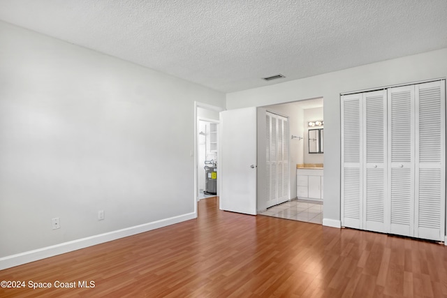 unfurnished bedroom with ensuite bathroom, a textured ceiling, and light wood-type flooring