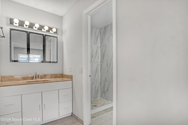 bathroom with tile patterned flooring, vanity, a textured ceiling, and tiled shower