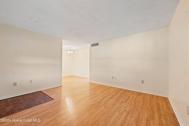 spare room featuring light hardwood / wood-style floors, a textured ceiling, and a chandelier