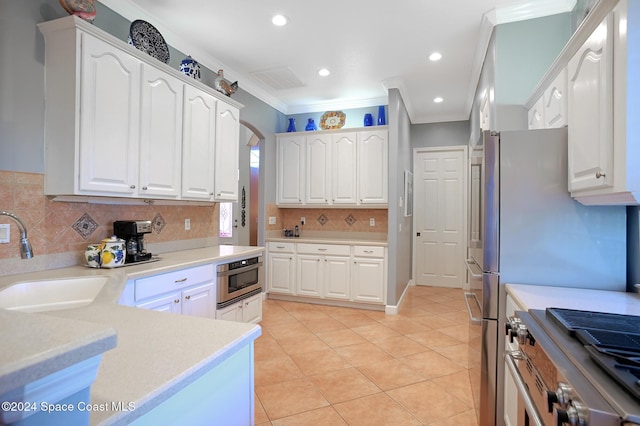 kitchen featuring white cabinetry, sink, appliances with stainless steel finishes, light tile patterned floors, and ornamental molding