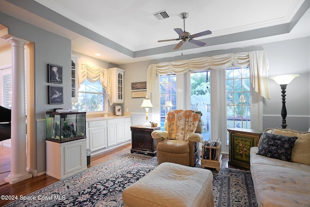 living room with dark hardwood / wood-style flooring, crown molding, a tray ceiling, and decorative columns