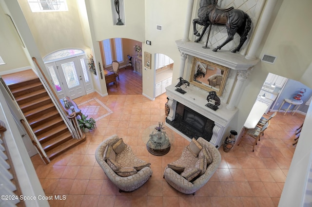 living room with a high end fireplace, a towering ceiling, and light wood-type flooring