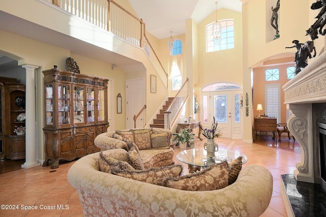 tiled living room featuring decorative columns, a premium fireplace, a chandelier, and a high ceiling