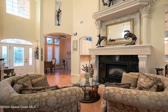 living room featuring a fireplace, a high ceiling, light tile patterned floors, and ceiling fan