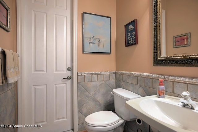 bathroom featuring toilet, tile walls, and sink