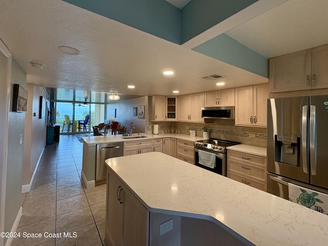 kitchen featuring kitchen peninsula, appliances with stainless steel finishes, decorative backsplash, light stone counters, and sink