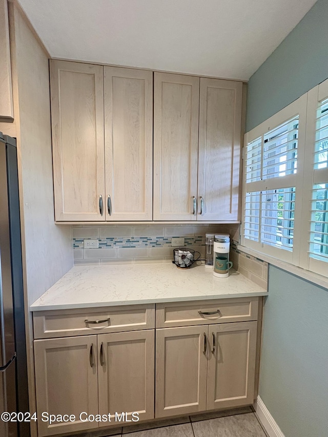 kitchen with decorative backsplash, light stone countertops, and stainless steel refrigerator