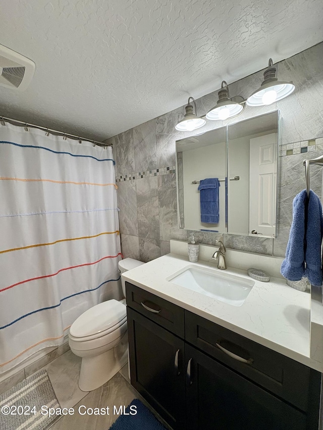 bathroom with a textured ceiling, vanity, toilet, and tile walls