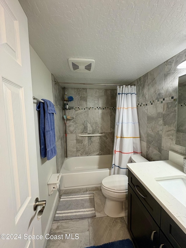 full bathroom with a textured ceiling, toilet, shower / tub combo with curtain, vanity, and tile walls