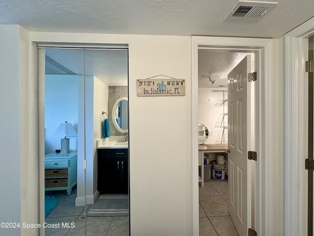 corridor featuring sink, light tile patterned floors, and a textured ceiling