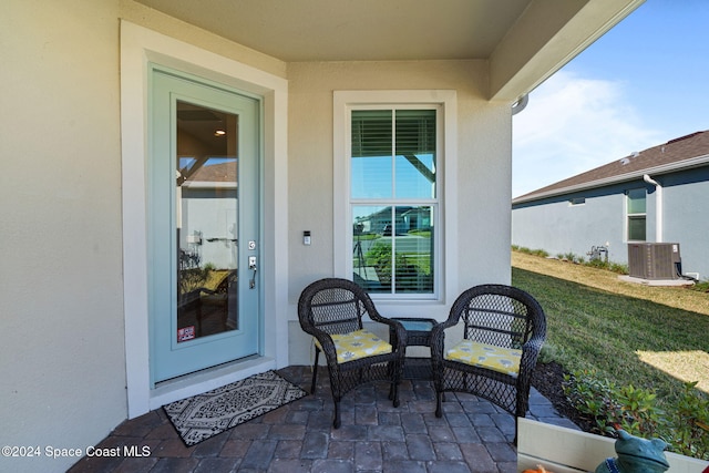 property entrance with central air condition unit, a lawn, and a patio