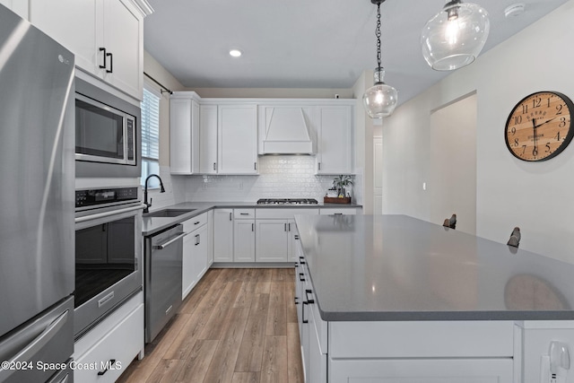 kitchen featuring appliances with stainless steel finishes, light wood-type flooring, custom range hood, sink, and white cabinets