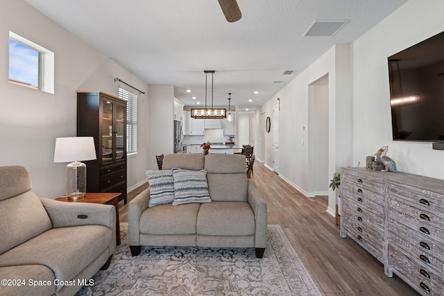 living room featuring ceiling fan, light hardwood / wood-style flooring, and a textured ceiling