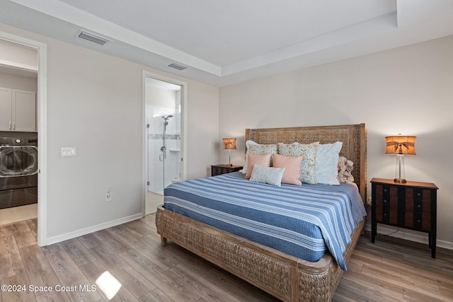 bedroom featuring washer / clothes dryer, hardwood / wood-style flooring, a tray ceiling, and ensuite bathroom