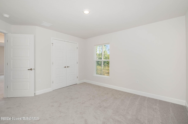 unfurnished bedroom with light colored carpet and a closet