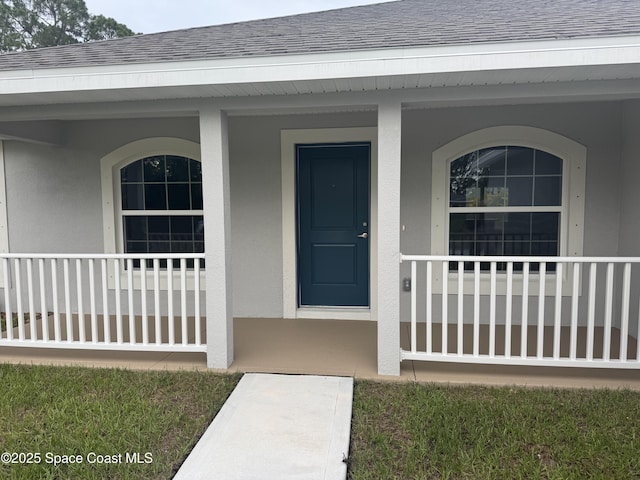 725 De Groodt Rd SW, Palm Bay, FL 32908 - view of exterior entry with a porch, stucco siding, and roof with shingles