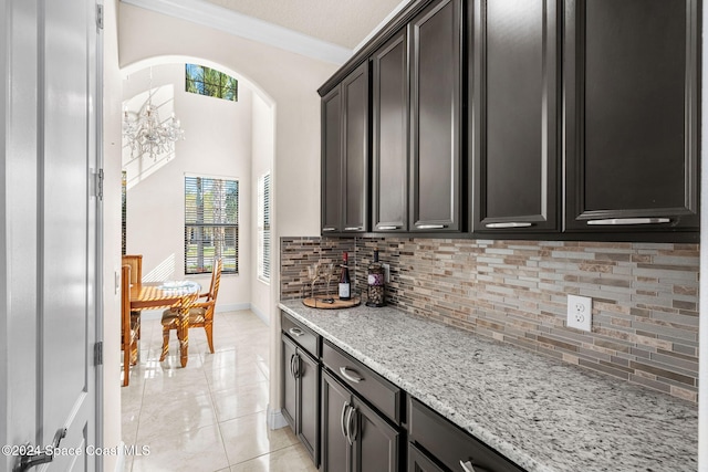 kitchen with decorative backsplash, light stone counters, ornamental molding, light tile patterned floors, and an inviting chandelier