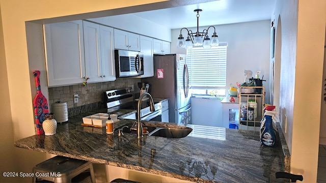 kitchen with white cabinets, appliances with stainless steel finishes, tasteful backsplash, and dark stone counters