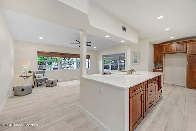 kitchen with light hardwood / wood-style floors, light stone counters, ceiling fan, and a kitchen island