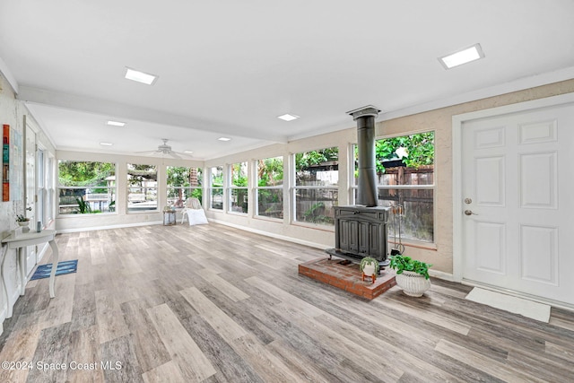 unfurnished living room with wood-type flooring, a wood stove, ceiling fan, and ornamental molding