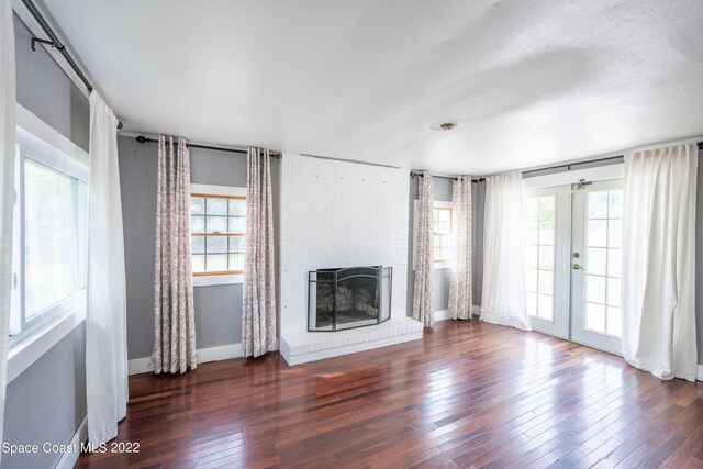 unfurnished living room with french doors, dark hardwood / wood-style floors, a brick fireplace, and plenty of natural light