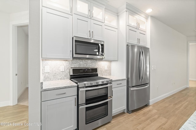 kitchen with light stone countertops, white cabinetry, light hardwood / wood-style flooring, and stainless steel appliances