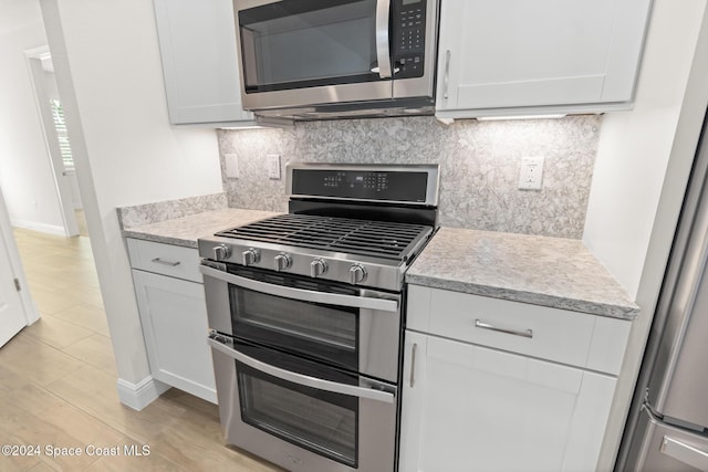 kitchen with decorative backsplash, white cabinetry, light hardwood / wood-style flooring, and stainless steel appliances