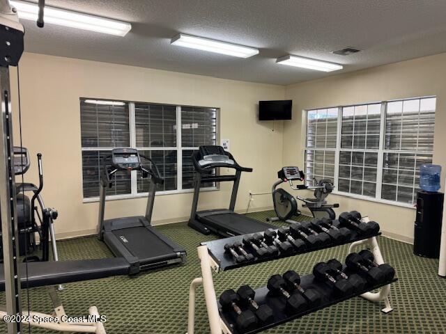 exercise room with dark colored carpet and a textured ceiling