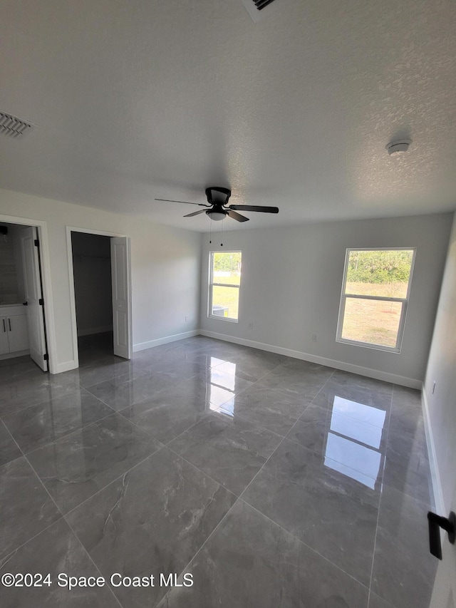 unfurnished room with ceiling fan, a healthy amount of sunlight, and a textured ceiling