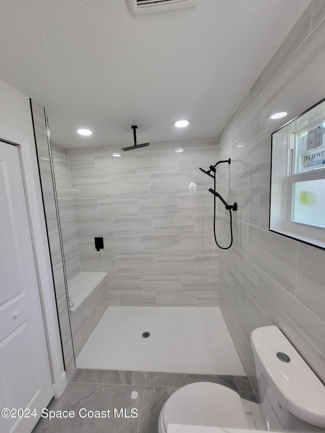 bathroom with a tile shower, toilet, tile walls, and tile patterned floors