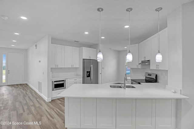 kitchen featuring kitchen peninsula, appliances with stainless steel finishes, light wood-type flooring, white cabinets, and hanging light fixtures