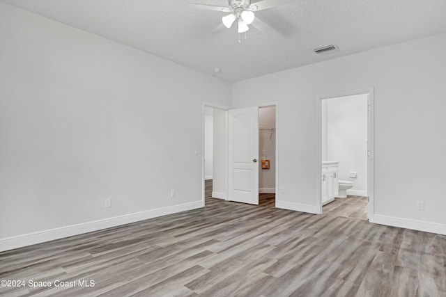 unfurnished bedroom featuring ceiling fan, a spacious closet, connected bathroom, light hardwood / wood-style floors, and a closet