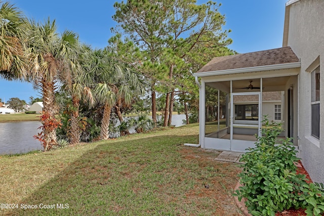 view of yard featuring a sunroom, ceiling fan, and a water view