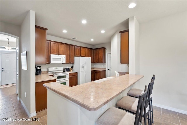 kitchen featuring a breakfast bar, white appliances, kitchen peninsula, and light tile patterned floors