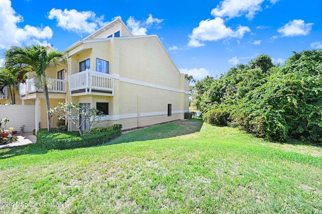 view of side of property with a balcony, a lawn, and stucco siding