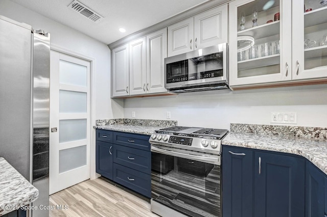 kitchen with light stone countertops, stainless steel appliances, blue cabinets, and light hardwood / wood-style floors