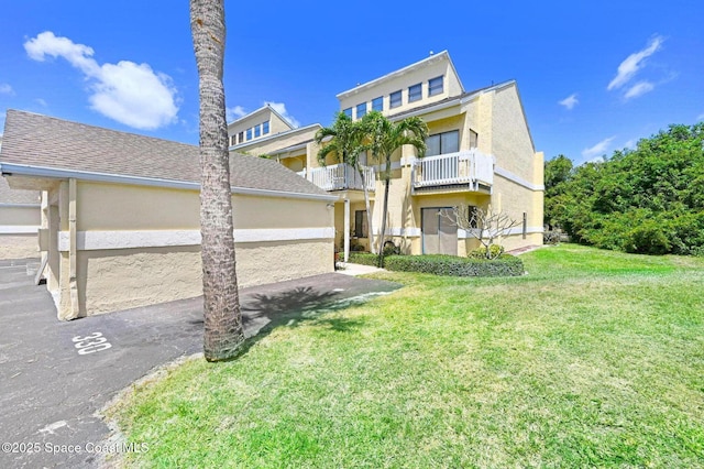 view of front of house with a balcony, stucco siding, and a front yard