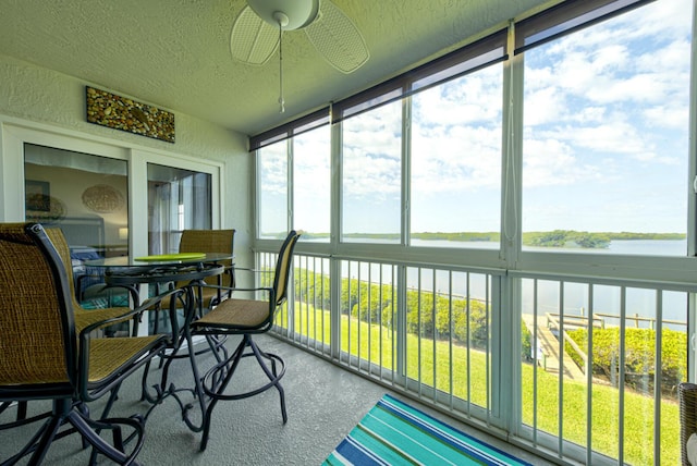 sunroom with ceiling fan and a water view