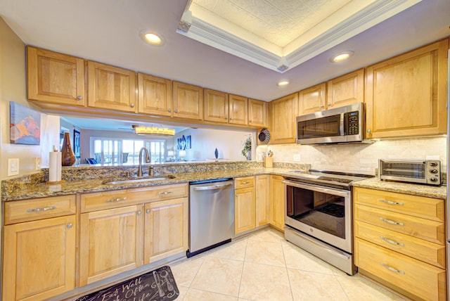 kitchen featuring appliances with stainless steel finishes, ornamental molding, a raised ceiling, sink, and stone countertops