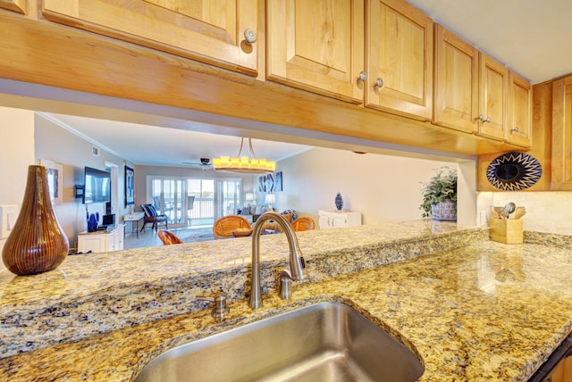 kitchen with light stone countertops, kitchen peninsula, ornamental molding, and sink