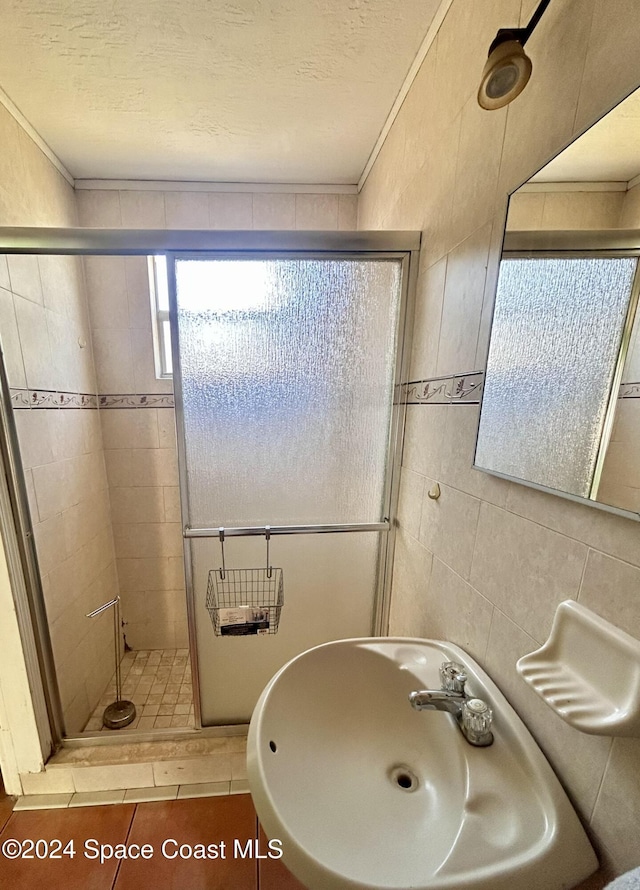 bathroom with tile patterned floors, sink, a shower with shower door, and tile walls