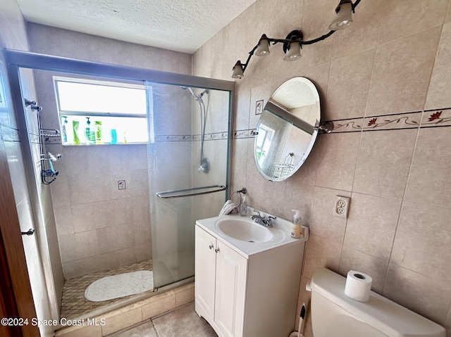 bathroom with vanity, a shower with shower door, a textured ceiling, and tile walls